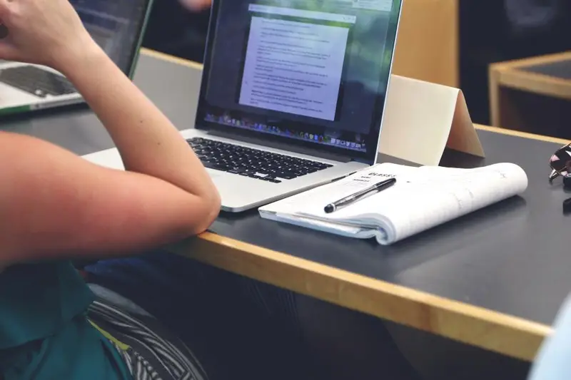 Estudiante con apuntes junto a un portátil en una mesa