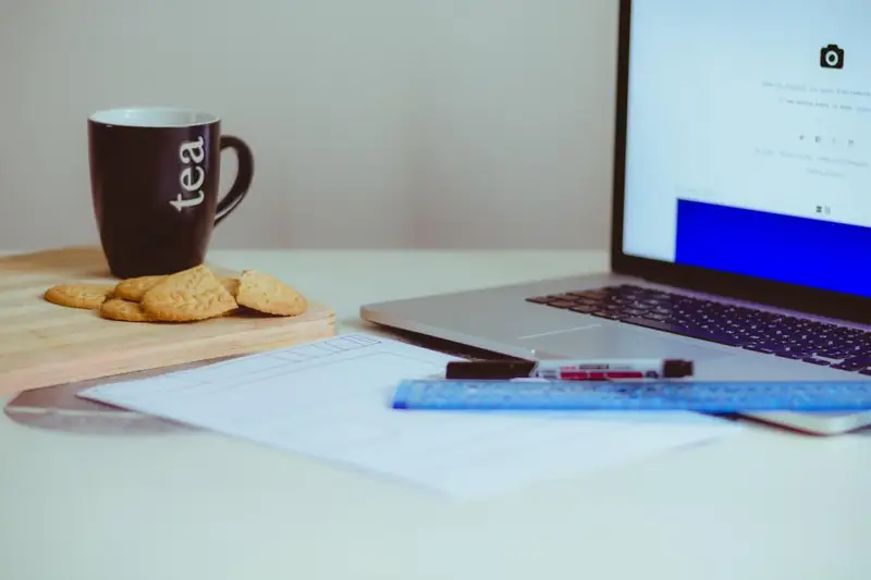 Portátil sobre una mesa junto a una taza de té y galletas