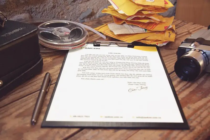 Documento firmado sobre una mesa junto a sobres y una cámara