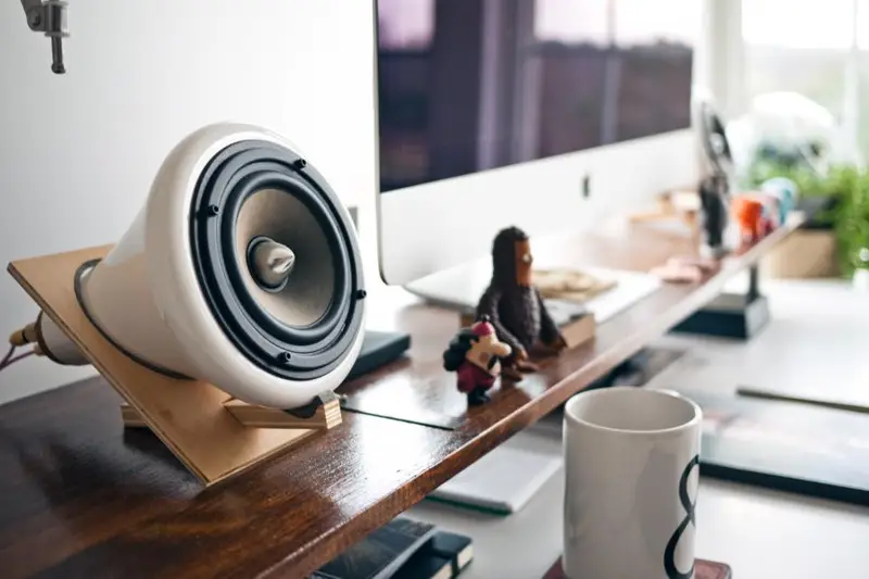Altavoz blanco sobre un escritorio junto a un monitor