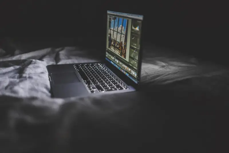 Portátil encendido sobre una cama en una habitación a oscuras