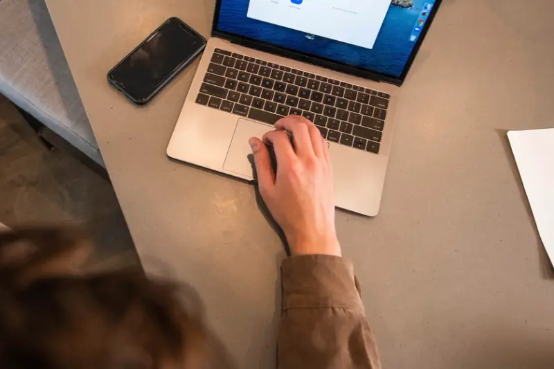 Manos usando un portátil sobre una mesa, junto a un móvil