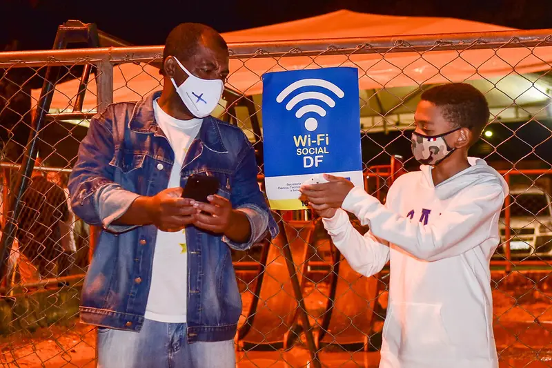 Dos personas mirando el móvil junto a un cartel de wifi público